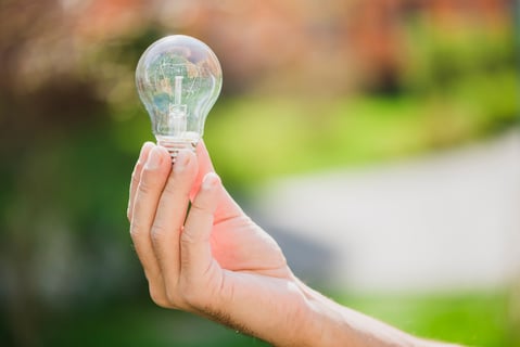 man-s-hand-showing-transparent-light-bulb-against-blurred-backdrop